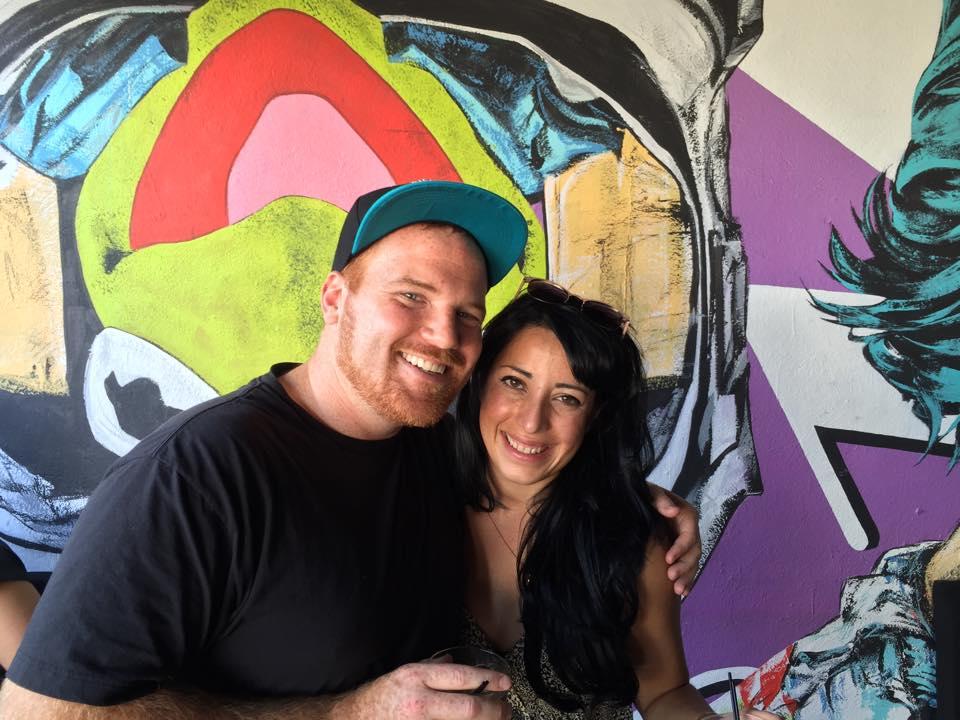 Man and woman smiling in front of colorful wall
